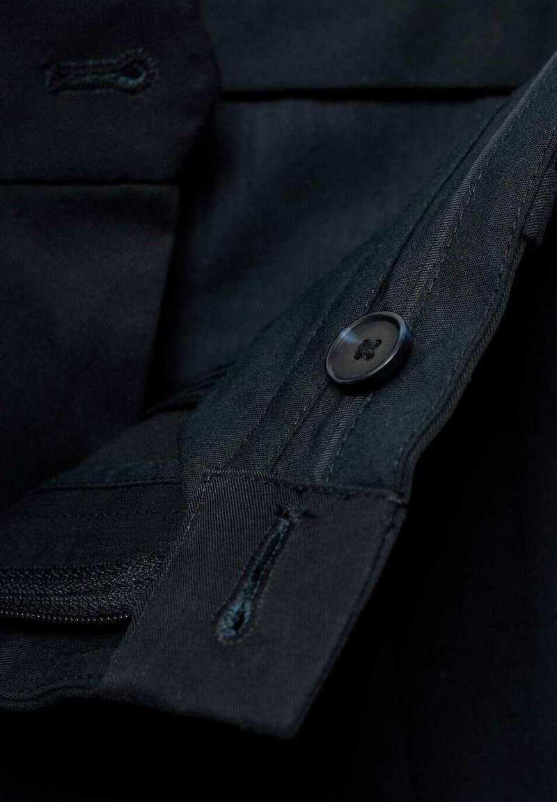 Schwarzer Stoff mit einer Taschenöffnung, ausgestattet mit einem Knopfverschluss und einem Reißverschluss. Die Textur ist glatt mit sichtbaren Nähdetails.
