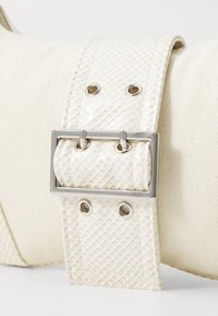 White faux leather belt with textured scales, silver hardware buckle, and eyelets. The material has a smooth finish with a subtle sheen.