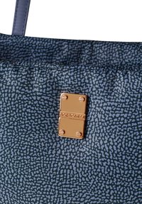 Borsa a tracolla in tessuto blu con motivo, dotata di un dettaglio in metallo rettangolare dorato lucido con il nome del marchio in rilievo. Texture liscia, design di media grandezza.