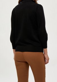 Svart pullovertröja med puffärmar och ribbad nederkant, i kombination med figurnära bruna byxor. Har en mjuk textur och en figursydd design.