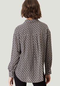 Sort-hvid mønstrede skjorte med et geometrisk design, lange ærmer og en knaplukket krave, med en afslappet pasform og buet kant.