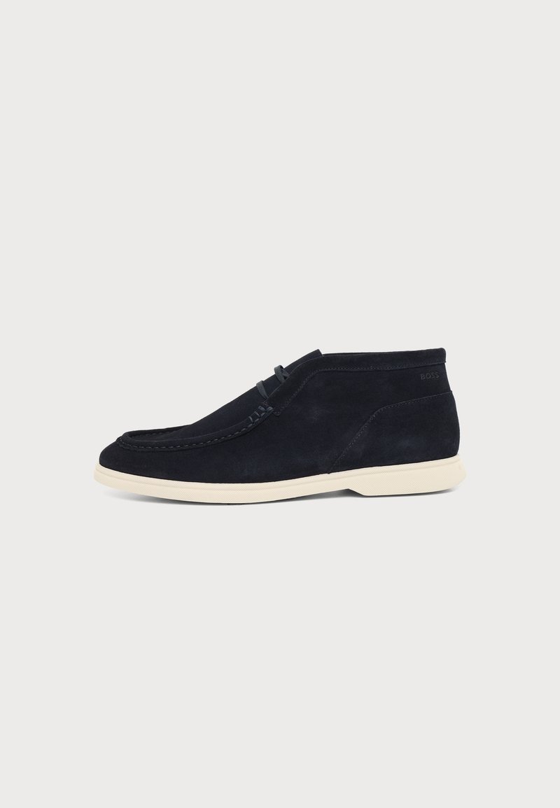 Chaussure décontractée montante mi-haute en suède noir avec semelle blanche et coutures apparentes sur fond clair uni.