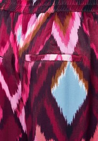 Multikleurige stof met een zigzagpatroon in tinten van roze, bordeaux, bruin en blauw, met twee zakken. Gladde textuur, elastische tailleband.