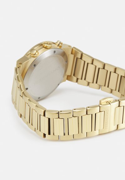 Orologio con finitura dorata, caratterizzato da un bracciale a maglie e una cassa rotonda. Il retro è liscio, con il nome del marchio inciso e tre pulsanti laterali.