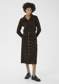 Brown corduroy midi skirt with front button closure and side pockets, paired with a dark brown knitted polo sweater and black loafers.