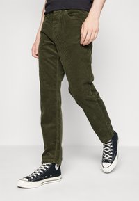 Groene corduroy broek met verticale ribbelstructuur, slim fit ontwerp en rechte pijpen. Gekoppeld aan zwarte hoge sneakers.
