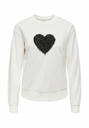 Fehér pulóver, középen texturált fekete szívvel. Hosszú ujjú, bordázott nyakkivágással és mandzsettákkal.