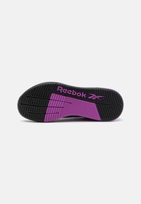 Fekete gumitalp rózsaszín kiemelésekkel és texturált tapadási mintákkal. A "Reebok" logó feltűnően lila színben van megjelenítve.