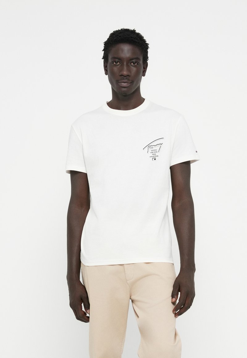 T-shirt en coton blanc avec manches courtes et col rond, présentant un logo imprimé noir sur la poitrine gauche. Texture lisse.