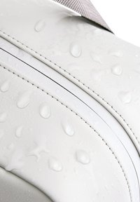 Borsa impermeabile bianca con una texture liscia, caratterizzata da gocce d'acqua, cuciture nere a contrasto e una tracolla grigia regolabile.
