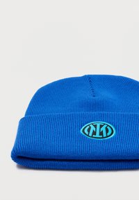 Πλεκτό μπλε σκουφί με ριγωτή υφή, με κυκλικό λογότυπο σε μαύρο και ανοιχτό μπλε στο μπροστινό μέρος. Σχεδίαση με διπλωμένο μανίκι.