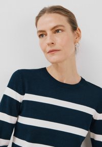 Maglione a maglia blu navy con ampie righe bianche, collo rotondo e polsini a coste. Presenta una texture leggera e una silhouette aderente.