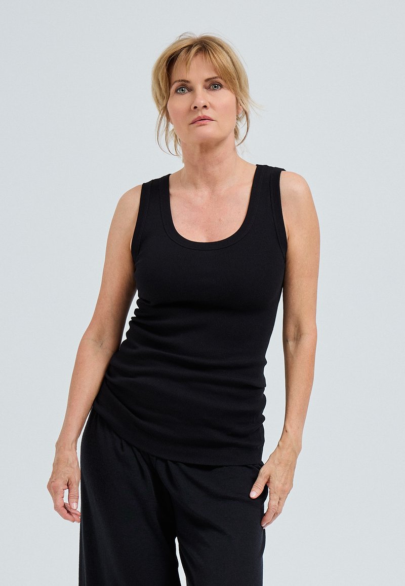 Zwarte geribbelde tanktop met een ronde hals en een getailleerd ontwerp. Huidskleurige broek maakt de outfit compleet en toont een gladde textuur.