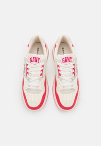 White sneakers with red accents, featuring a perforated toe cap and prominent "GANT" branding on the tongue and side. Textured fabric materials.