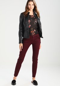 Sorte læderjakke over en blomsterstrikket top, parret med bordeaux slim-fit bukser og sorte slip-on sko. Enkel, strømlinet design.