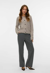 Ljust grå, fluffig cardigan med rak form och rund halsringning, prydd med svarta knappar. Matchad med grå byxor med lätt rand och klackar.