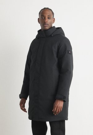 Schwarze Kapuzenparka mit Reißverschluss, weichem Material und verstellbaren Bündchen. Mit einem Logoschild auf dem linken Ärmel.