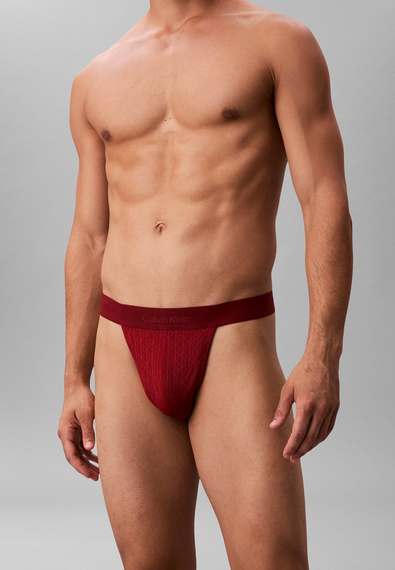 Roter Calvin Klein Tanga aus weichem Material, mit einem strukturierten Diamantmuster und einem logo-prägierten Bund, im Tiefschnitt-Design.