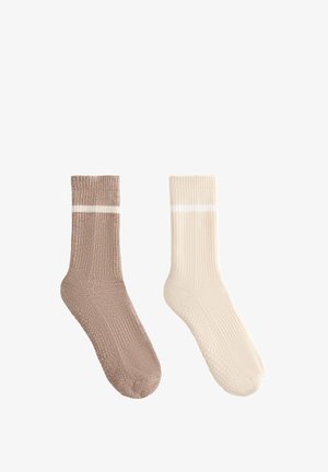 Ribbyt neuleputket vaaleassa ruskeassa ja kermassa, joissa on valkoiset raidat. Pehmeä pinta ja vaimennetut pohjat mukavuutta varten.