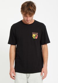 Sort bomulds t-shirt med et farverigt grafisk motiv på venstre bryst med blomster- og dyremotiver; afslappet pasform og rund hals.