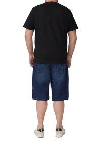 Schwarzes Baumwoll-T-Shirt, Shorts aus dunkelblauem Denim, knielang mit zwei Gesäßtaschen, kombiniert mit weißen Sneakers mit Akzenten.