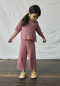 Roze gebreid twee-delig outfit met een kortmouwtop met een geschulpte zoom en ruime broek met een decoratieve rand. Gecombineerd met gele schoenen.