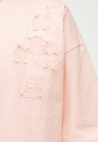 Ανοιχτόροζ ύφασμα με δύο υφασμάτινα σχήματα σταυρού ραμμένα με νήμα στο ίδιο χρώμα στην άνω περιοχή του στήθους ενός ενδύματος.