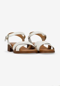 Sandalias de cuero blanco con correas cruzadas y una pequeña hebilla, que presentan un tacón bajo marrón y un acabado texturizado en las correas.