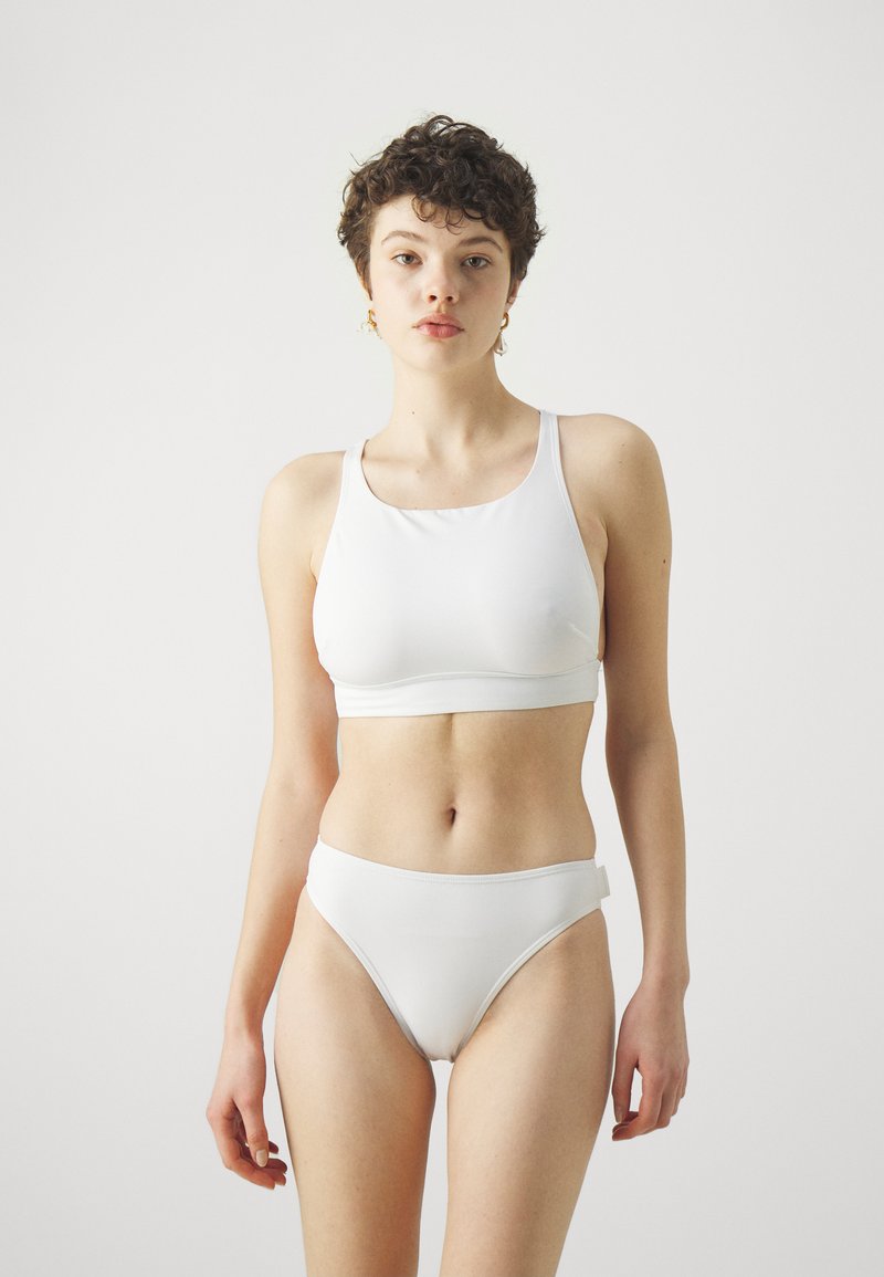 Biely bikiny set s výstrihom doá a širokými ramienkami, doplnený o zodpovedajúce vysoké spodky. Vyrobené z hladkej, elastickej tkaniny.