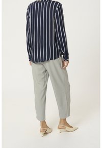 Person, der ein navyblaues und weißes, vertikal gestreiftes Langarmhemd, hellgraue Hosen und beigefarbene Slingback-Kitten-Heels trägt und mit dem Rücken zur Kamera steht.