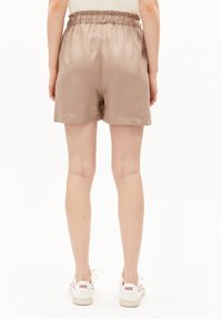 Satin beige shorts with an elastic waistband, smooth texture, and a relaxed fit, worn with white sneakers featuring red accents.