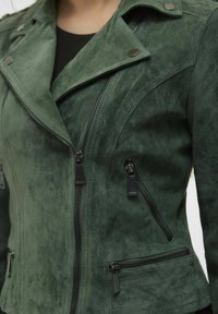 Grüne Kunstwildleder-Motorradjacke mit silbernen Beschlägen, Reißverschlusstaschen und asymmetrischem Revers. Weiche Textur und taillierte Passform.