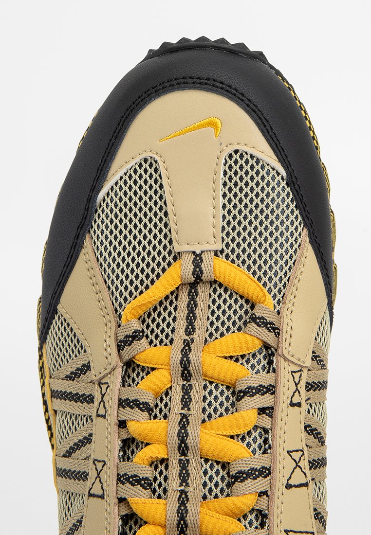 Beżowo-czarne siatkowe sneakersy z żółtymi akcentami, teksturowaną powierzchnią i wyraźnym logo Nike. Zawierają szczegółowy system sznurowania.