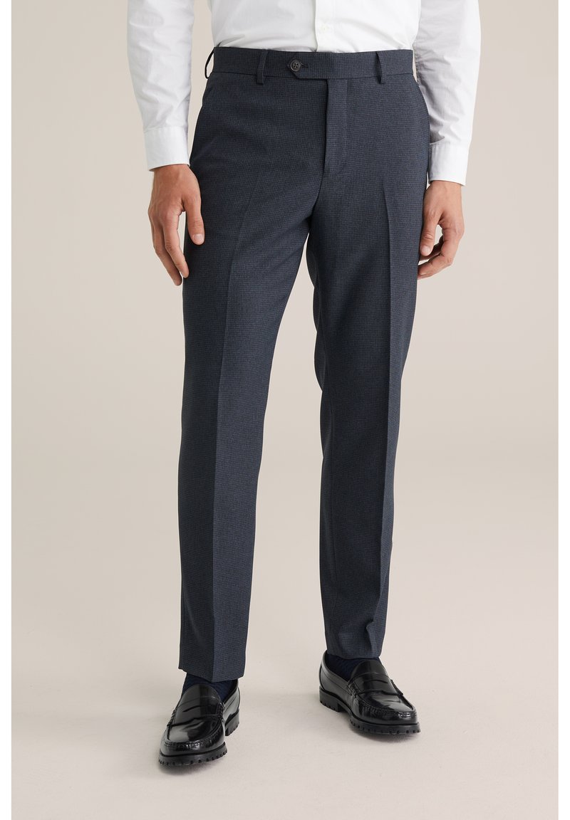 Jūras zila rūtainas bikses ar piegrieztu piegulumi, gludu tekstūru un vienu pogas aizdari, kopā ar melniem loaferiem.