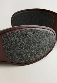 Suela de zapato de goma con un agarre texturizado negro, con un borde suave marrón. La vista en primer plano enfatiza la forma y los detalles de la superficie.