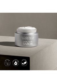 Open pot Doctor Babor Collagen-Peptide Booster Cream op een beige oppervlak, met zicht op de crèmetextuur en productlabels.