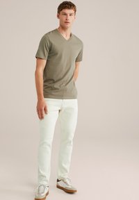 Olivno zelen majica s V izrezom, prilegajoča zasnova. V kombinaciji z belimi ravnimi hlačami in nizkimi čevlji na vezalke v beli in bež barvi.