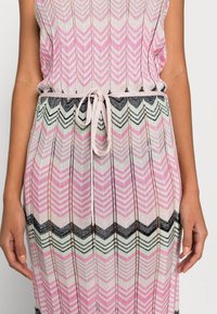 Klänning i stickat med ett zigzag-mönster i rosa, grönt och svart. Den har ett knyt i midjan och strukturerad tyg med öppen väv.