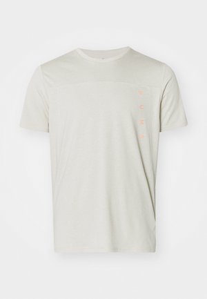 T-shirt beige clair à manches courtes avec un panneau supérieur texturé et le logo "PUMA" en orange sur le côté gauche. Coupe régulière avec un col rond.