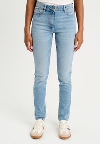 Lysblå denim skinny jeans har en høj talje og et klassisk fem-lomme design. De er parret med hvide og brune lave sneakers.