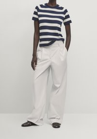 Striped, navy and white knit t-shirt with a round neckline, paired with high-waisted, wide-legged, light gray trousers and flat sandals.