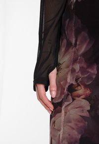Schwarzes Mesh-Kleid mit langen Ärmeln und floralem Druck. Verfügt über Daumenlöcher, eine glatte Textur und eine seitliche Naht, die das Design betont.