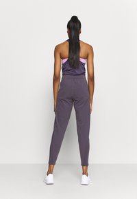 Sportovní outfit s tmavě fialovým topem a růžovými akcenty, doplněný úzkými kalhotami. Materiál vypadá hladce a elasticky, v kombinaci s bílými botami.
