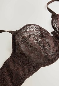 Barna csipkés melltartó virágmintákkal, állítható pántokkal és félig áttetsző kosarakkal, világos felületen laposan elhelyezve.