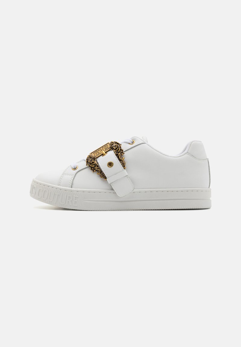 White leather sneaker with a gold decorative buckle, flat sole, and embossed branding on the side. Laces are white, with minimal stitching details.