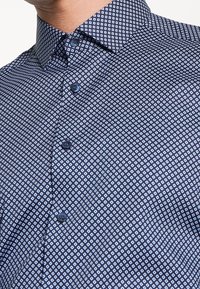 Camicia blu navy con motivo geometrico a quadrati bianchi, colletto button-down e bottoni piatti, realizzata in tessuto leggero.