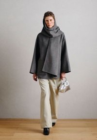 Hall hall vildist mantel pikkade varrukatega, rippuva kraega ja ees taskutega. Sobitatud helebeež laia laiusega pükstega ja mustade kingadega, hoides hõbedast kotti.