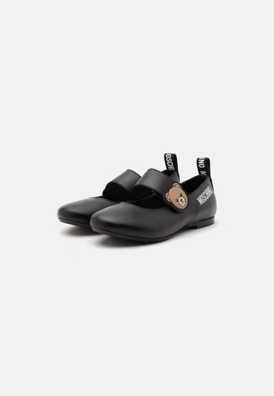 Chaussures Mary Jane noires avec un détail visage d'ours sur la bride et des languettes de traction à la marque au talon sur un fond blanc uni.