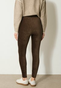 Bruine corduroy leggings met een strakke pasvorm, gecombineerd met een beige sweater en witte sneakers. De textuur is zacht met verticale ribbels.