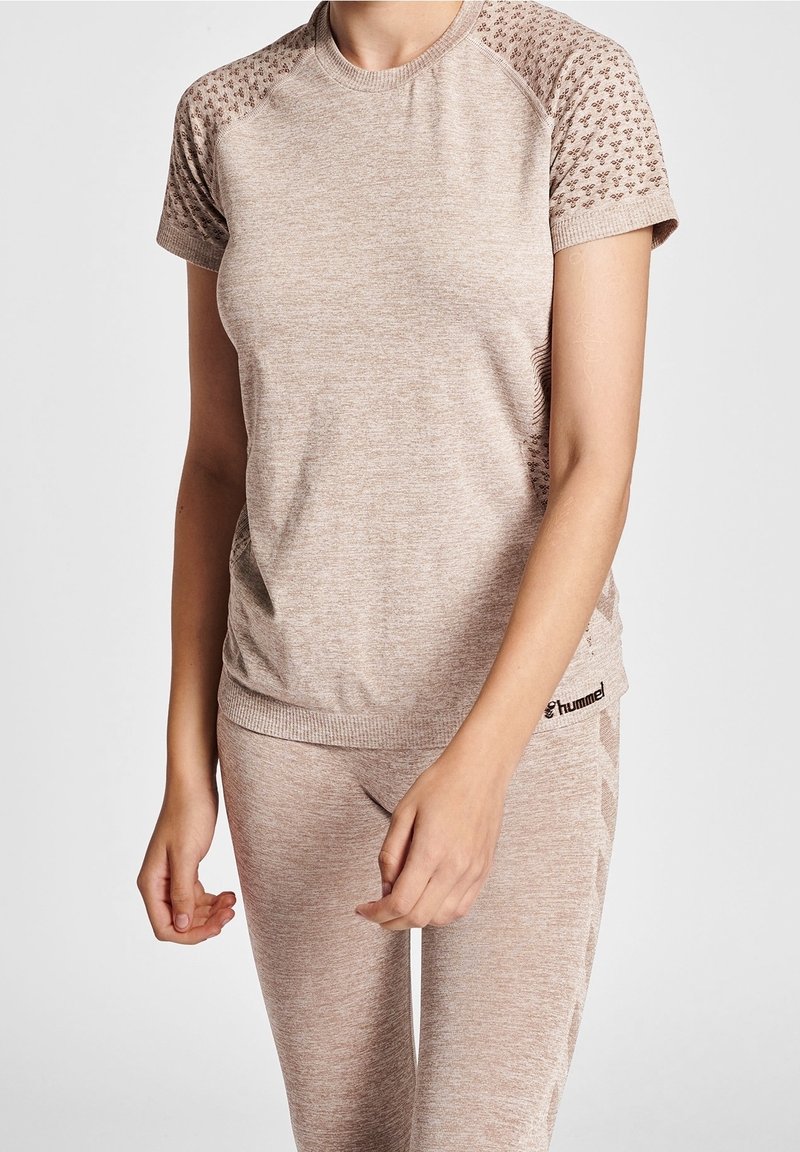 Camiseta deportiva marrón claro con mangas cortas, patrón texturizado en los hombros y cuello acanalado. La tela es suave y elástica.